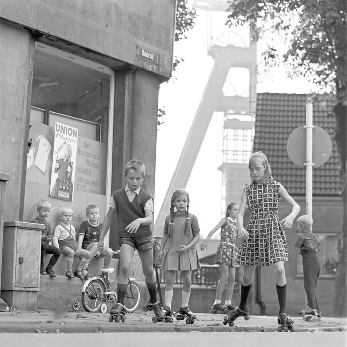 Rollschuh laufende Kinder auf der Saarstraße, Herne-Sodingen. Im Hintergrund ein Fördergerüst von Zeche Mont Cenis, um 1970. LWL/Helmut Orwat (vergrößerte Bildansicht wird geöffnet)